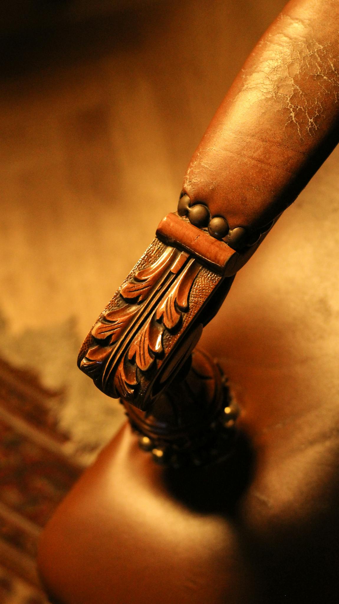 Detailed shot of a carved leather armrest on a classic armchair in warm lighting.